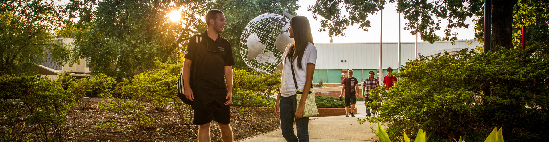 Students walking in front of globe structure in setting sun